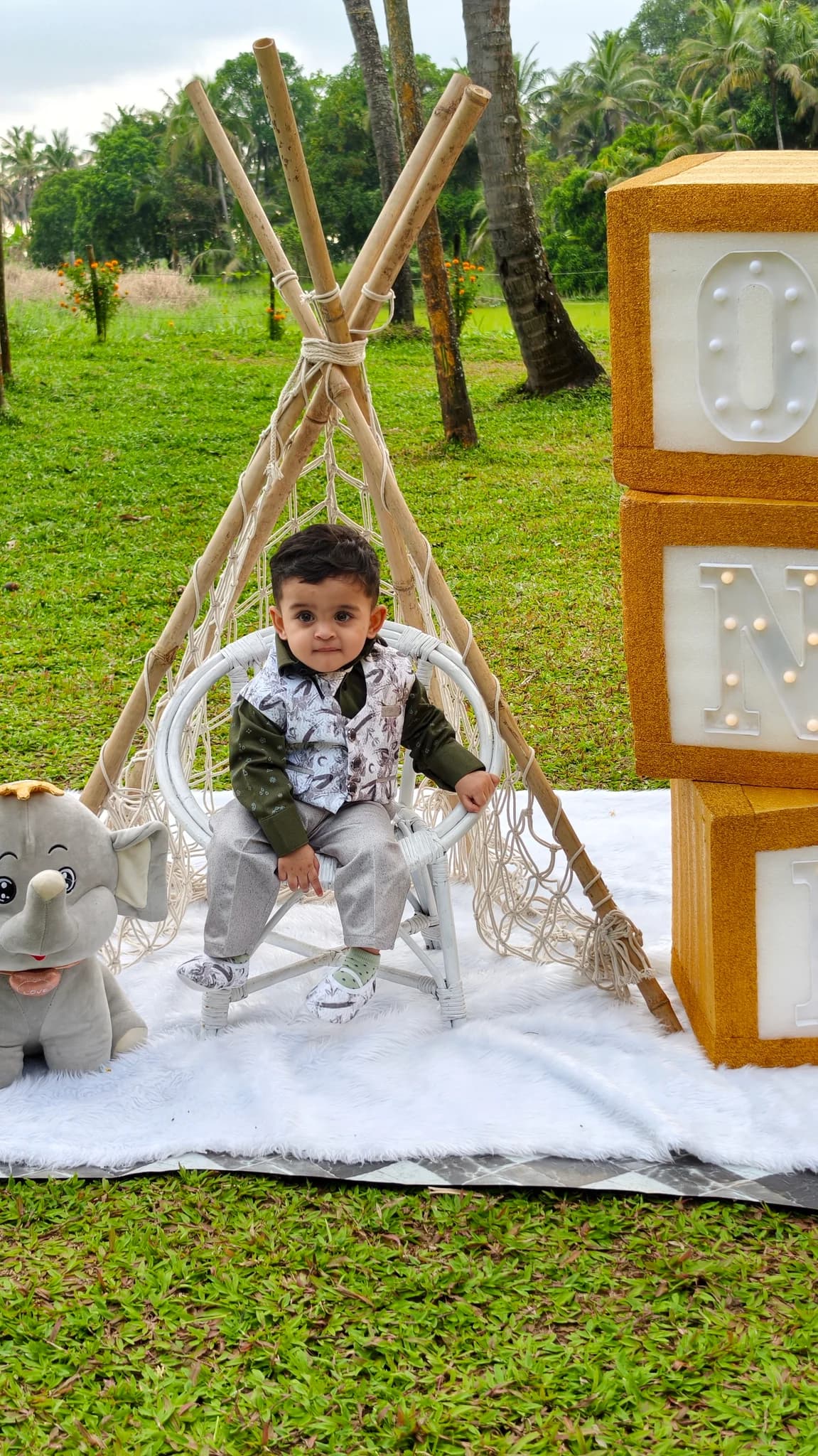 Child seated in a white wicker chair at a garden birthday photo spot in Thrissur